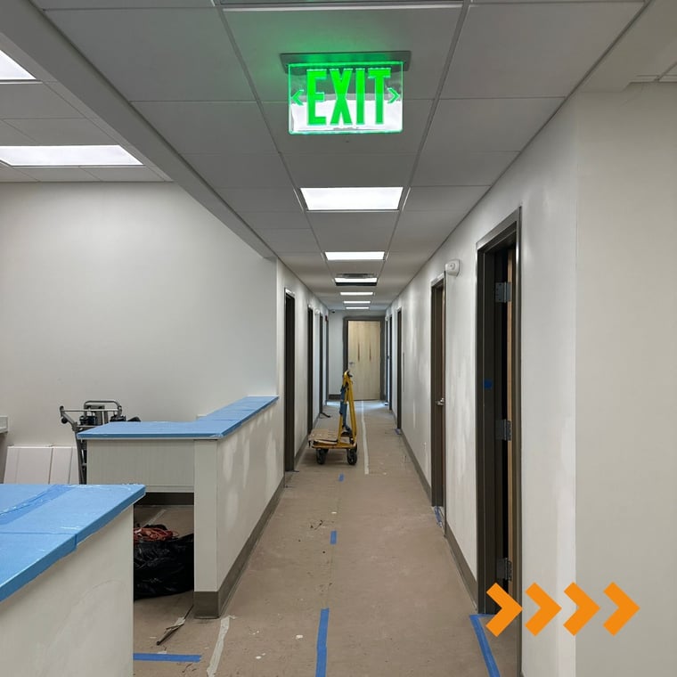 This is an image from Coastal Painting Contractors company, located in Naples, FL. The image is an interior commercial hallway under renovation with fresh wall paint and protective coverings, Coastal Painting Contractors project