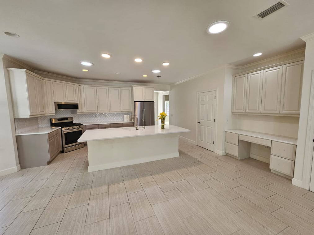 This is an image from HH Painting company, located in Gainesville, FL. The image is a modern kitchen with freshly painted white cabinets, large island, and built-in desk area with light tile flooring