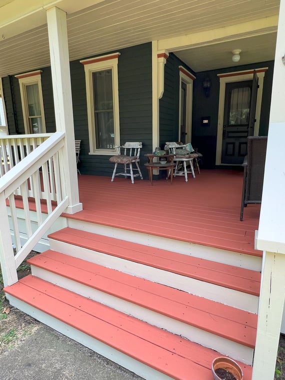 This is an image from Brushmen and Standby Bros company, located in Lansing, MI The image is a freshly painted Victorian-style front porch with redwood-colored steps, cream trim, and deep green siding, exterior painting by Brushmen and Standby Bros