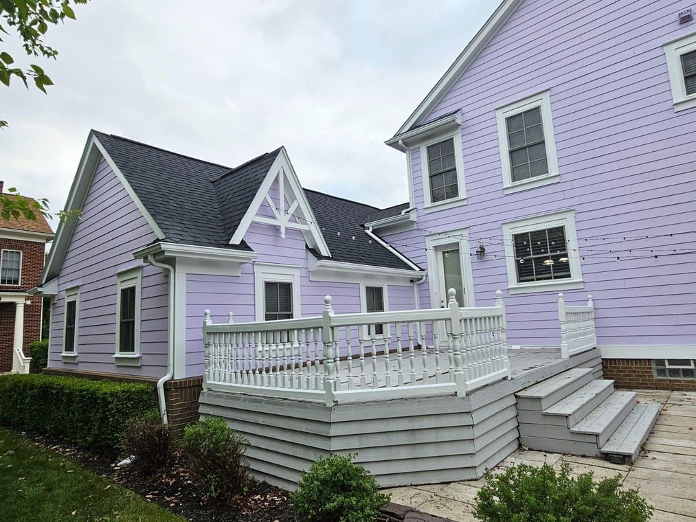 This is an image from MacFarland Painting - Ann Arbor company, located in Ann Arbor, MI The image is a two-story home painted in lavender with white trim and gray deck, completed by MacFarland Painting.