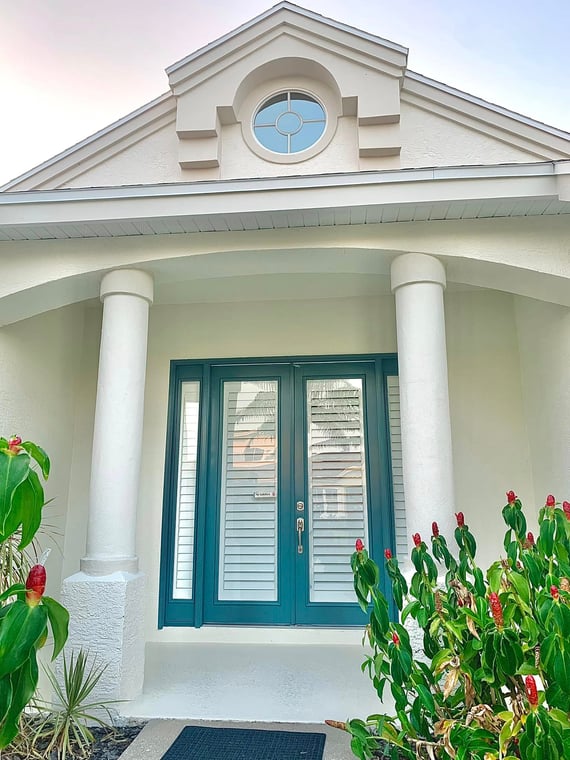This is an image from Color It Up Painting company, located in Bradenton, FL. The image is a front entryway of a stucco home with freshly painted teal double doors, white columns, arched entry, and circular window above.