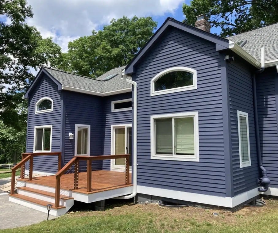 This is an image from Blue Mountain Painting, located in Massachusetts. The photo shows a modern home with freshly painted navy blue siding, white trim, and a wooden deck, creating a bold and polished exterior look.