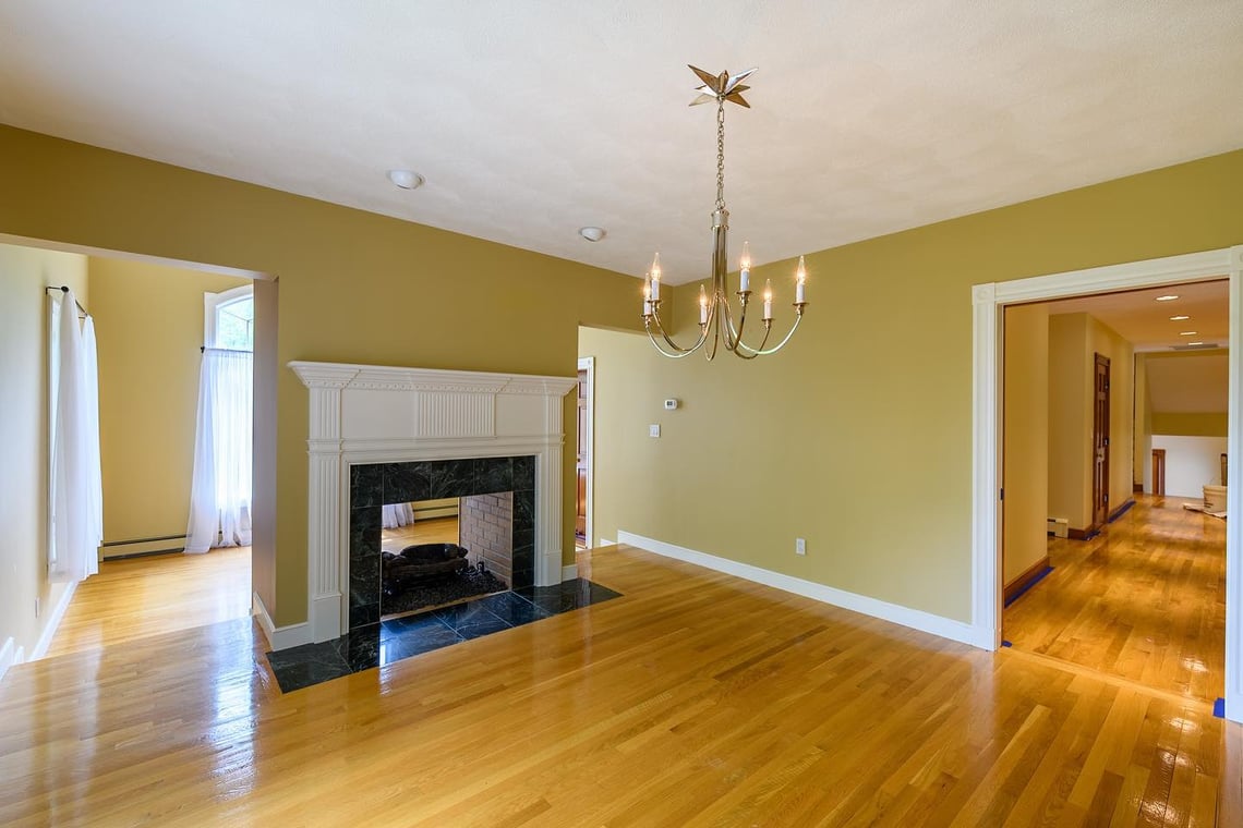 Interior dining room painted by Jose's Painting Co., showing golden yellow walls, polished hardwood floors, a central chandelier, and a decorative fireplace with a black marble surround.