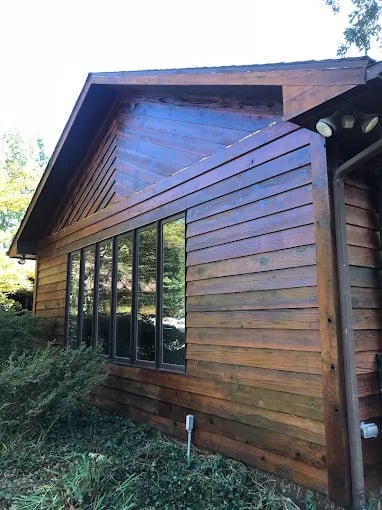 This is an image from Graham's Painting company, located in Du Quoin, IL The image is a stained and sealed wood siding on a residential home with large windows, showcasing exterior wood restoration and finishing by Graham's Painting 