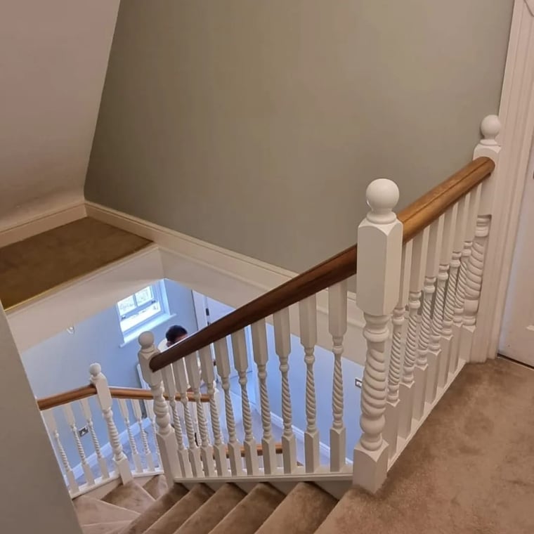 This is an image from Sir Paints A Lot company, located in Eugene, OR The image is an interior staircase painting by Sir Paints A Lot with freshly painted white spindles, polished wood handrail, and neutral wall colors in a modern home.