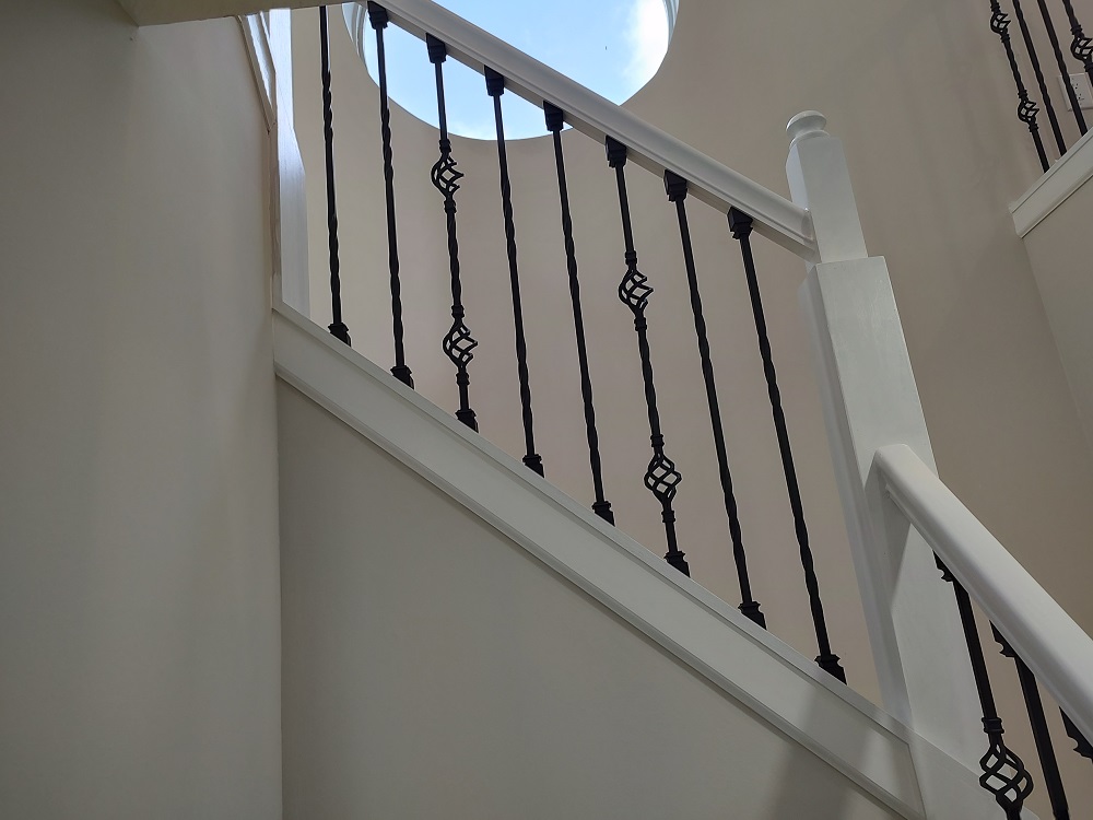 This is an image from Promax Painters company, located in Boynton Beach, FL. The image is a freshly painted stairwell with white walls and decorative black wrought iron balusters under circular skylight