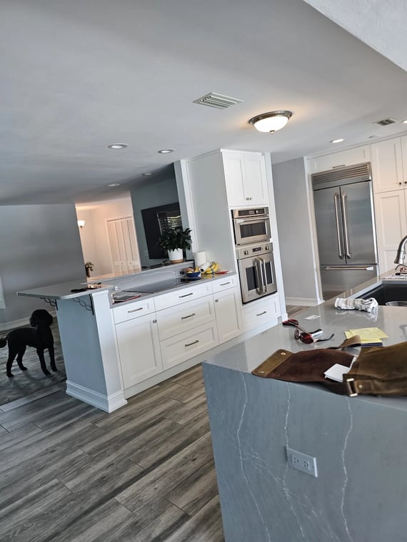 This is an image from Nu Trend Painting Inc. company, located in St. Petersburg, FL. The image is a modern kitchen renovation with white shaker cabinets, stainless steel appliances, gray quartz countertops, and wood-look tile flooring