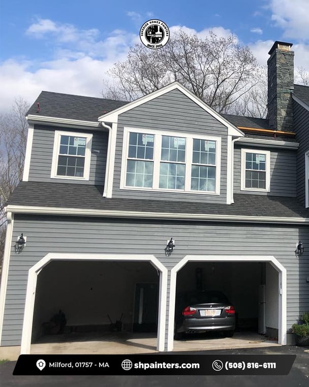 This is an image from Superior Homes Painters, located in Massachusetts. It shows a gray house exterior with white trim and a two-car garage, highlighting fresh siding and trim painting.