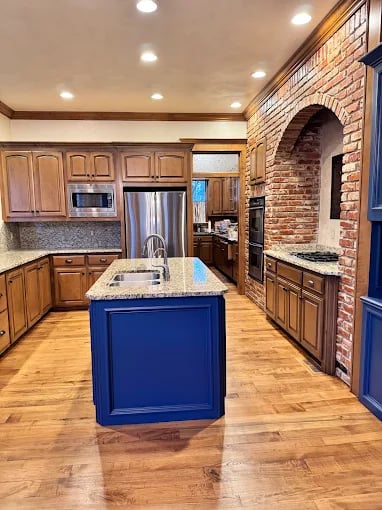 This is an image from Fixable Painting, located in Oklahoma City, Oklahoma. The photo shows a remodeled kitchen with natural wood cabinets, a bold blue island, stainless steel appliances, and a brick archway feature.