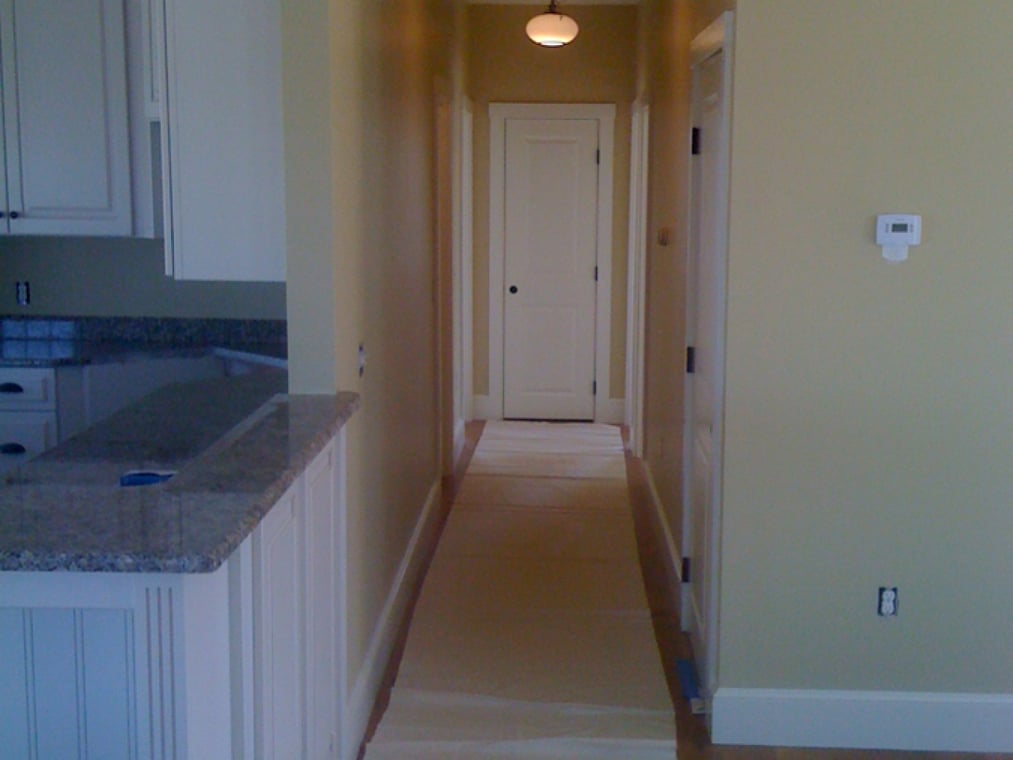 This is an image from Nelson Painting, Inc., located in Massachusetts. It shows exterior painting work on a large beige home with a lift being used to reach the upper sections of the siding.