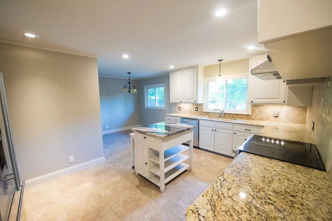 This is an image from Straight Line Paint & Remodeling, located in Oklahoma. The photo shows a modern kitchen remodel with granite countertops, white cabinetry, tile flooring, and a small center island.