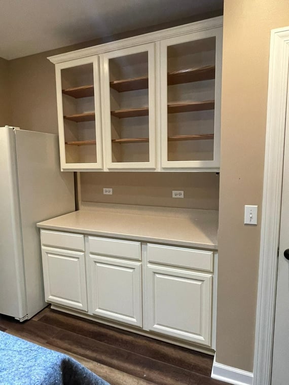This is an image from Epic Painting, LLC company, located in Bull Valley, IL The image is a custom-painted white kitchen cabinets with glass-front upper doors and beige countertops in a modern home interior
