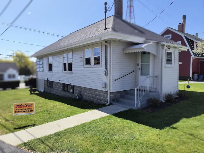 This is an image from CertaPro Painters of Attleboro, MA. It shows a freshly painted light gray single-story home with white trim and a neatly cut lawn.