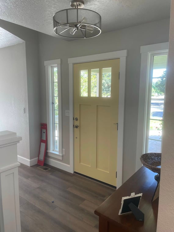 This is an image from Horizon Painting LLC company, located in Boise, ID The image is a modern entryway with soft yellow painted front door, gray walls, white trim, and wood-look vinyl plank flooring
