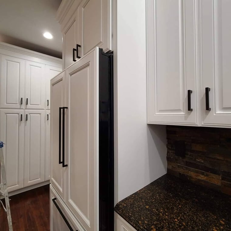This is an image from Great Lakes 1-800 Painting LLC company, located in Davison, MI The image is a modern kitchen with freshly painted white cabinets, black hardware, dark granite countertops, and stacked stone backsplash.