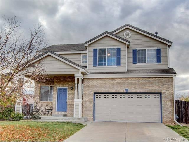 This is an image from Parker CO Painter, LLC company, located in Parker, CO The image is a  two-story suburban home with tan brick facade, beige siding, and blue shutters, featuring a blue front door and attached two-car garage – exterior painting by Parker Painting in Parker, Colorado
