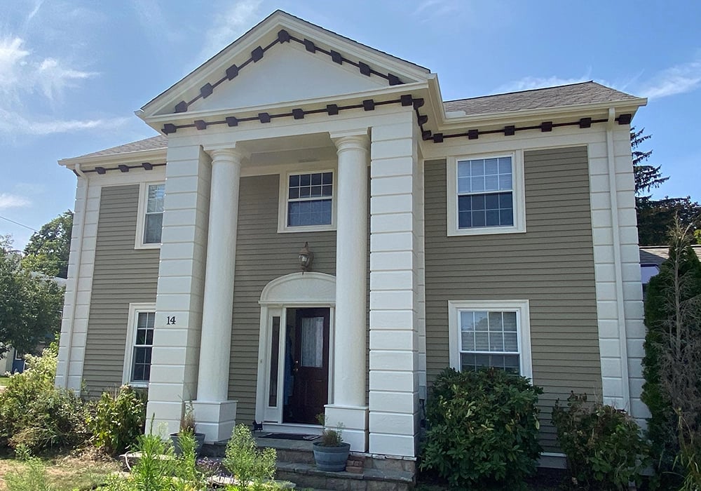 This is an image from Zuck Painting, located in Massachusetts. It shows the exterior of a two-story home with beige siding, large white columns, and neatly painted trim.