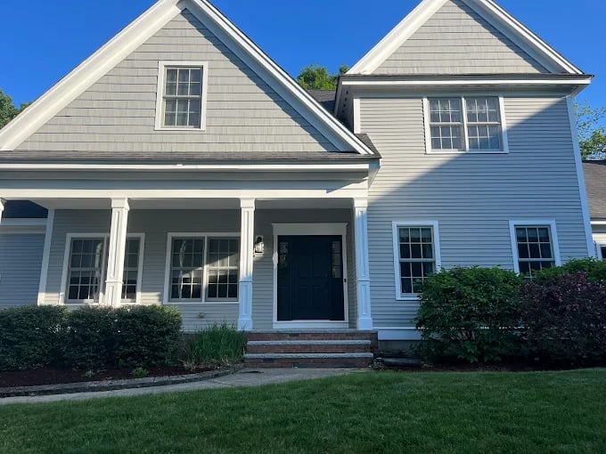 This is an image from CertaPro Painters, showing a freshly painted two-story gray house with white trim and a black front door. The clean siding and neat landscaping highlight the crisp finish.