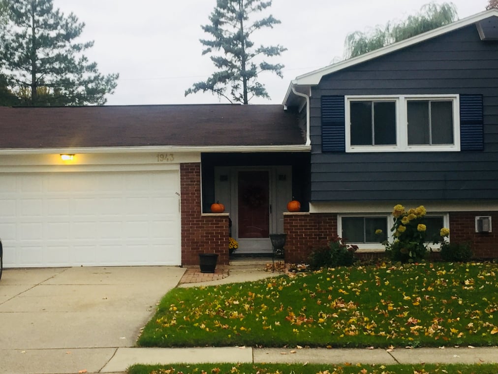 This is an image from Paint Master Painting Inc company, located in Lansing, MI The image is a single-story beige vinyl-sided house with white trim and gable roof, freshly painted exterior by PaintMaster Painting