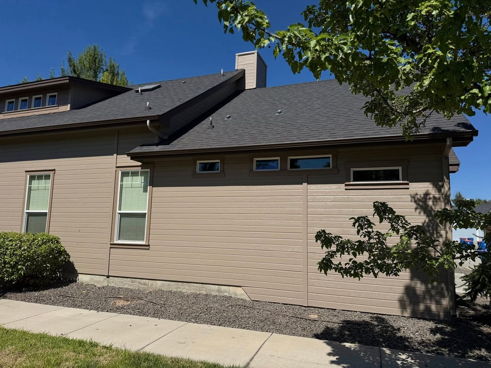 This is an image from Montenegro's Painting & Construction LLC company, located in Meridian, ID The image is a side view of a modern home with freshly painted tan horizontal siding, dark shingle roof, white-trimmed windows, and manicured landscaping, exterior painting by Montenegro's Painting & Construction, LLC