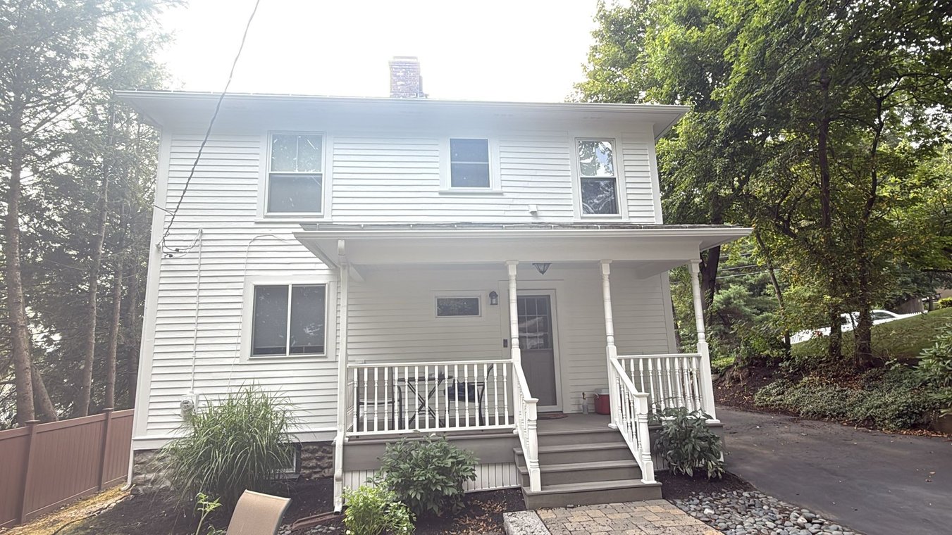 This is an image from Moura Quality Painting, located in Massachusetts. It shows the exterior of a freshly painted two-story white home with a covered porch and updated trim.