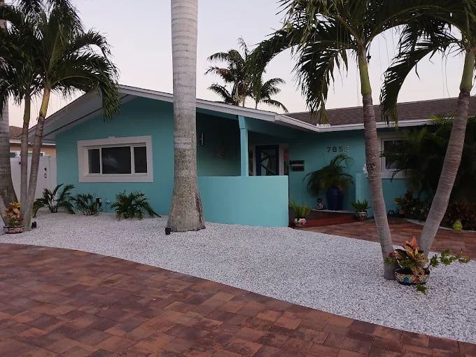 This is an image from Pinellas County Painting company, located in St. Petersburg, FL. The image is a freshly painted light blue coastal home with white trim, palm trees, and brick driveway in Pinellas County, Florida.