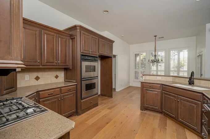 This is an image from Hometown Painting, located in Oklahoma. The photo shows a spacious kitchen with dark wood cabinets, light granite countertops, hardwood flooring, and built-in double ovens.