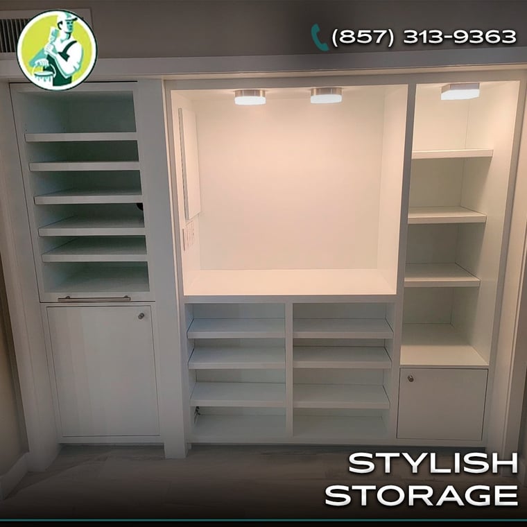 This is an image from Lou's Painting Company, located in Massachusetts. The photo shows a custom-built white storage unit with shelving, cabinets, and overhead lighting, designed for a clean and stylish interior space.