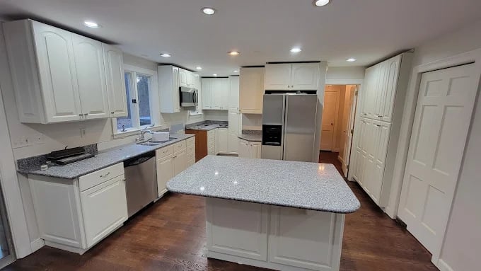This is an image from Fresh Coat Painters of Andover, located in Massachusetts. The photo shows a modern kitchen with freshly painted white cabinets, granite countertops, and stainless steel appliances.