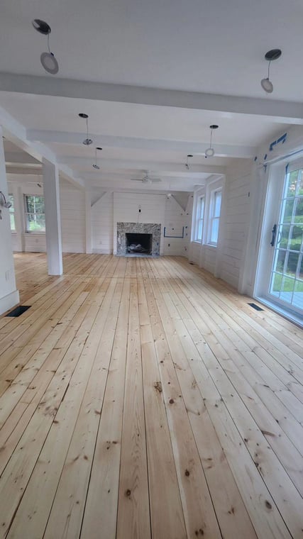 This is an image from Leo's Painting and Carpentry Services, located in Massachusetts. The photo shows a freshly renovated living room with light wood plank flooring, white painted walls, and a stone fireplace as the centerpiece.