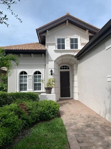 This is an image fromAncient Modern Finishes company, located in Bonita Springs, FL. The image is a freshly painted Mediterranean-style home exterior with white walls, dark trim, and arched windows by Ancient Modern Finishes