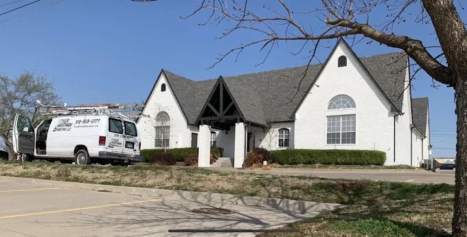 This is an image from Tyler Hoffman Painting, LLC. The photo shows a bright white-painted commercial-style building with steep gables, a parking lot in front, and the company’s branded van parked nearby.