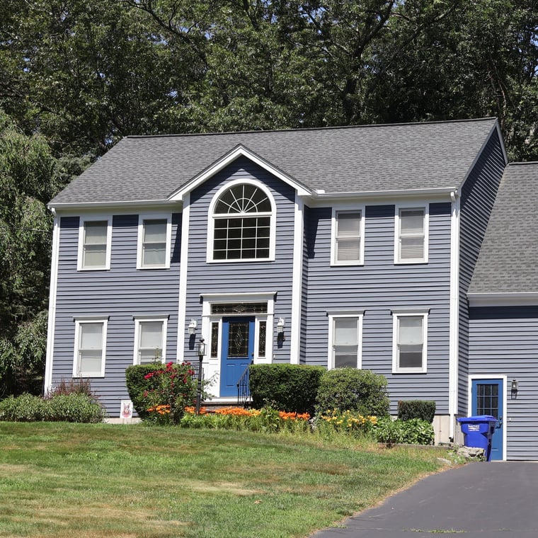 This is an image from CertaPro Painters of the Upper Charles, located in Massachusetts. It shows a two-story colonial-style home with navy blue siding, white trim, and a bright blue front door.