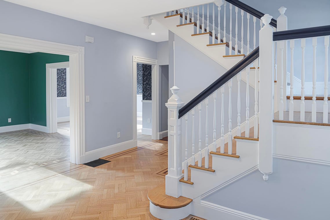 This is an image from Gonnella Painting & Restoration, located in Massachusetts. It shows a freshly painted stairwell with white railings, dark handrails, and soft blue-gray walls.