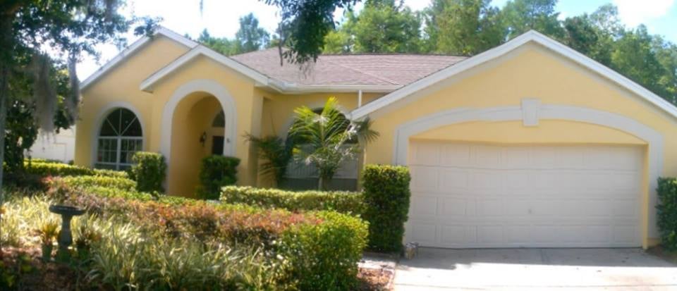 This is an image from Debaggis Painting company, located in Orlando, FL. The image is a freshly painted yellow exterior of a single-story suburban home with white trim and a two-car garage, by DeBaggis Painting