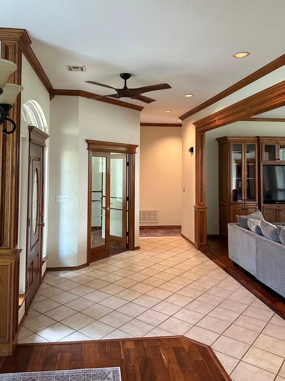 This is an image from Cardinal Painting, located in Oklahoma. The photo shows a freshly painted interior with cream-colored walls, wood trim accents, tiled flooring, and a transition into a living area with wood flooring and built-in cabinetry.