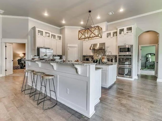 This is an image from Whitehead Brothers Painting, located in Oklahoma. The photo shows a modern kitchen with freshly painted white cabinets, stainless steel appliances, and a large island with granite countertops and bar seating.