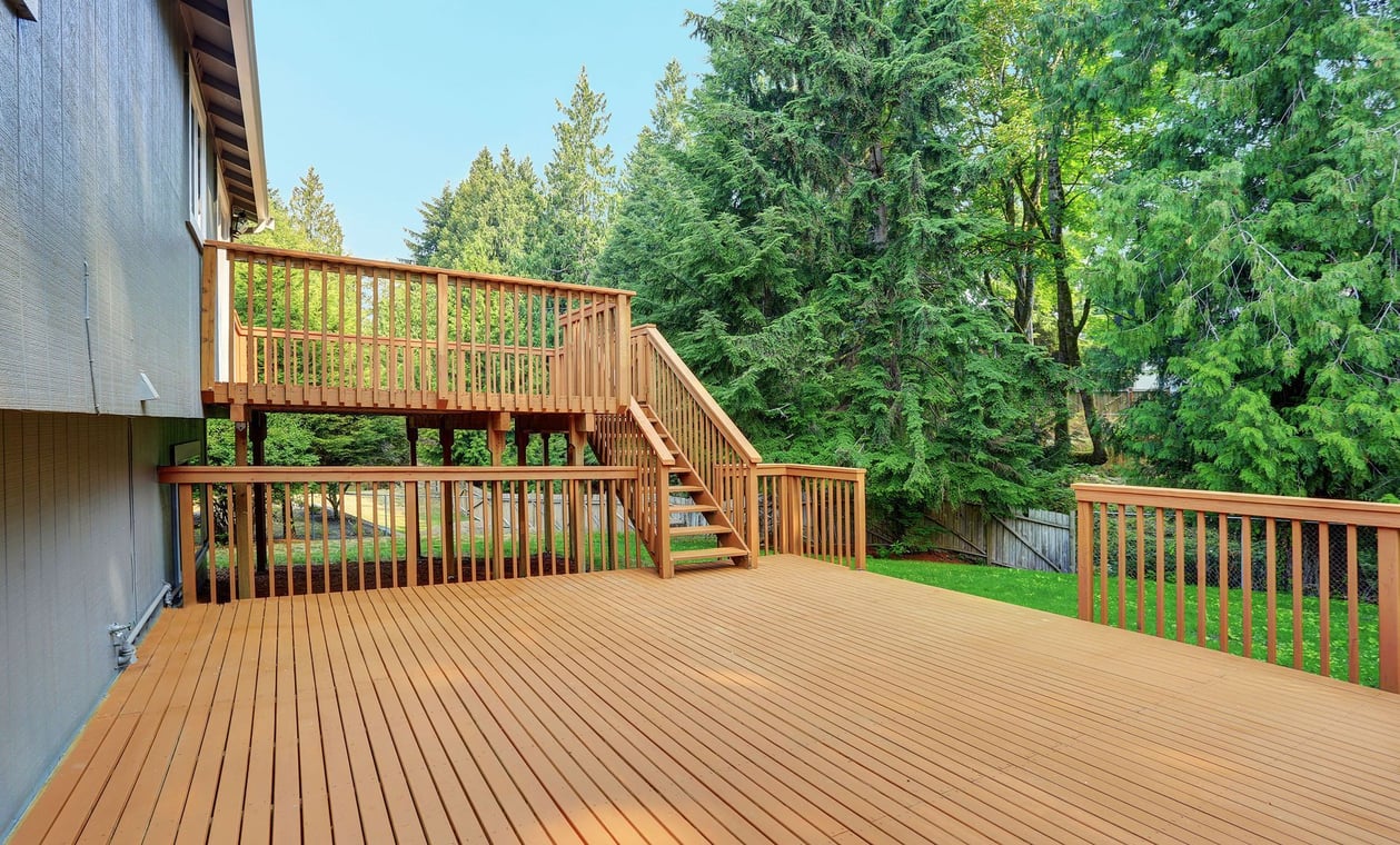 This is an image from All Painting Plus 2, LLC company, located in Colorado Springs, CO The image is a freshly stained wooden backyard deck with stairs and railings by All Painting Plus 2 LLC, professional deck staining and exterior painting services.