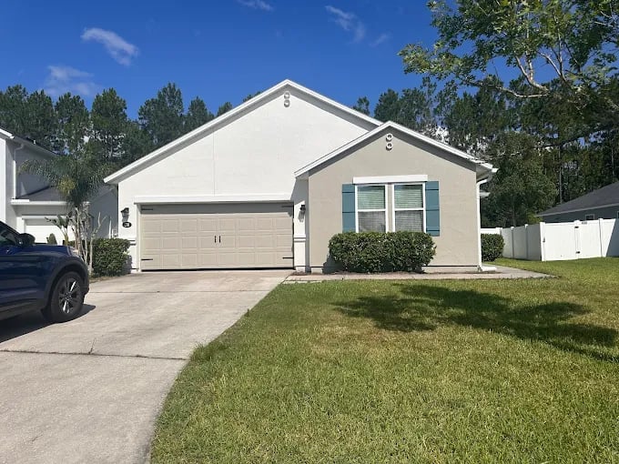 This is an image from Rockstar Painting, Inc. company, located inJacksonville, FL. The image is a freshly painted single-story home with light gray exterior, white trim, and blue shutters, completed by Rockstar Painting Inc. in a suburban neighborhood.
