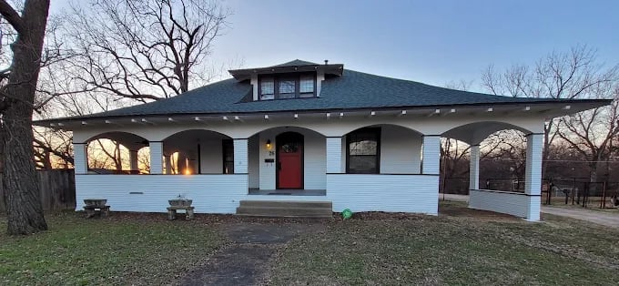Exterior of a white house with a wide wraparound porch and a red front door, freshly painted by Groovy Hues Painting of Tulsa.