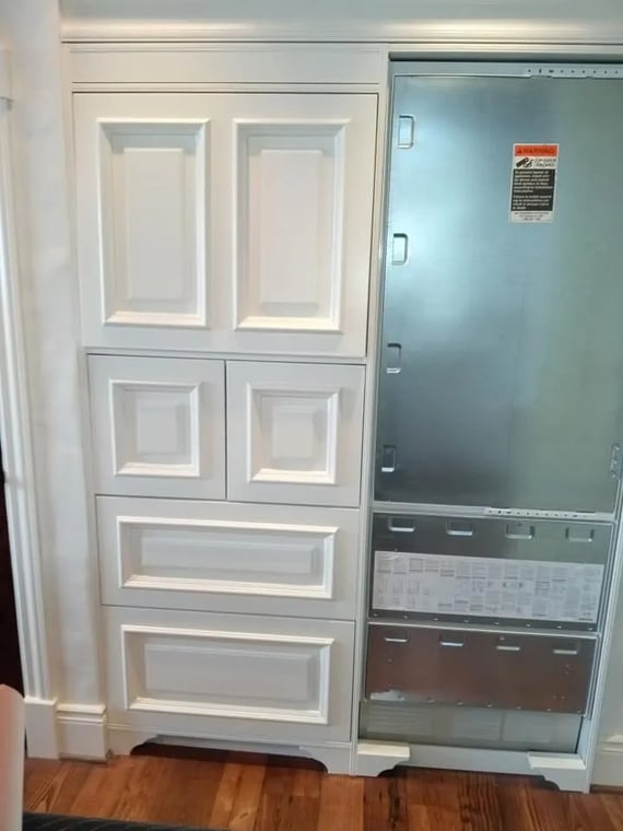 This is an image from RLS Painting company, located in Boyne City, MI The image is a custom cabinet painting project with white paneled cabinetry installed around a metal electrical panel, blending functional and decorative elements with clean trim work.