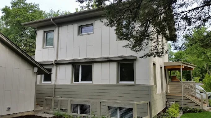 This is an image from Artisons Painting And Remodeling Hinsdale Painters IL company, located in Brookfield, IL The image is a two-story home with modern exterior painted in light beige and gray by Artisons Painting and Remodeling, surrounded by trees and greenery