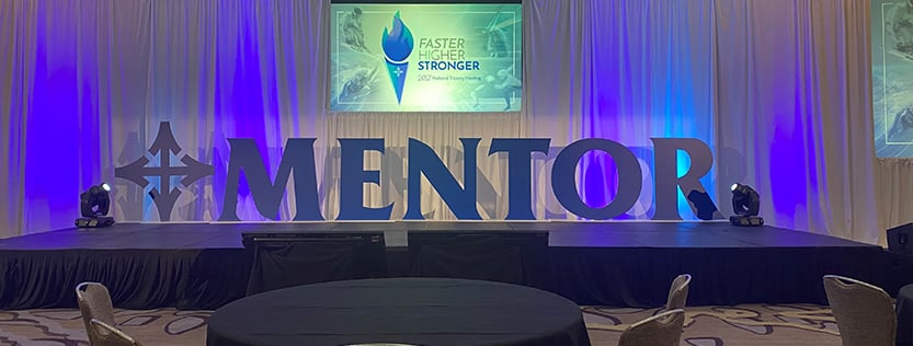 Custom cut oversized letters reading "Mentor" displayed on stage.