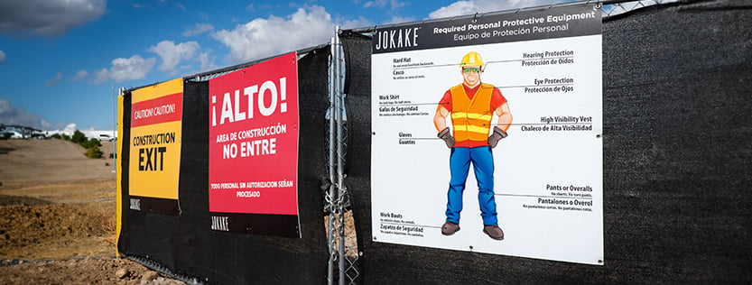 Construction safety signs hung on a fence at a building site.