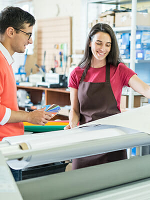 Мужчина и женщина рассматривают образцы красок рядом с большим рулоном печатной бумаги.