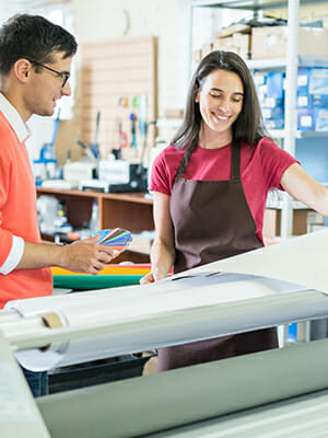 Man and woman looking at color samples beside a large roll of printing paper.