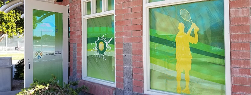 Entrance to a brick building with window graphics for tennis.