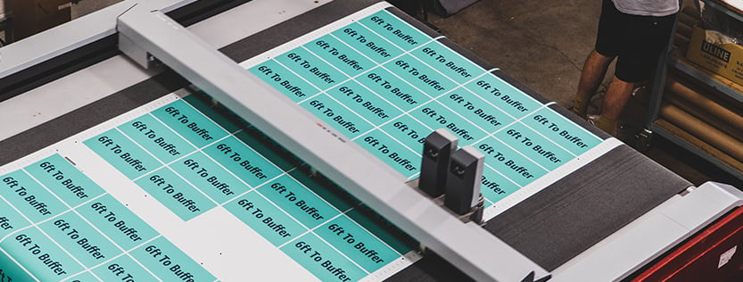 Aerial view of a precision cutting machine cutting out teal rectangular labels.