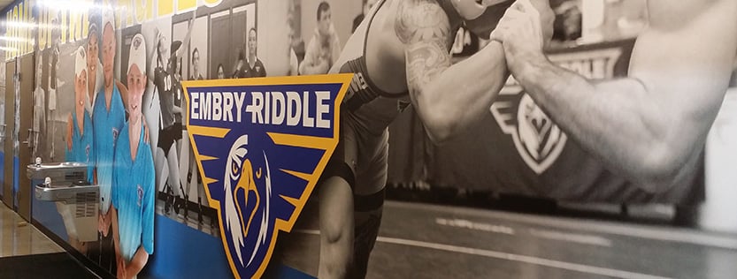 large printed wall mural or various college sports athletes with a dimensional school logo sign.