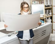 Young woman standing at a printing looking over a printed project.
